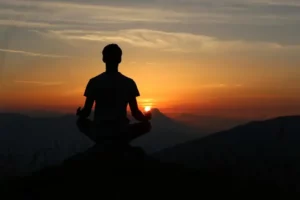 une personne de dos qui fait de la méditation devant un coucher de soleil